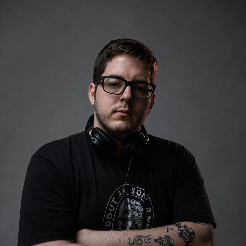 Retrato do DJ Lipe de braços cruzados, com fone no pescoço
